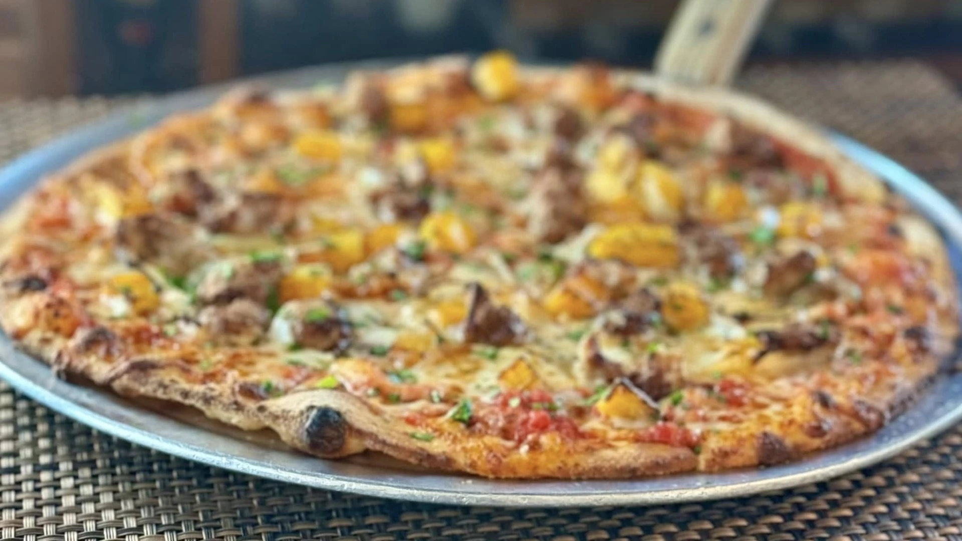 Wood-fired pizza topped with sausage, roasted squash, herbs, and melted cheese on a metal tray