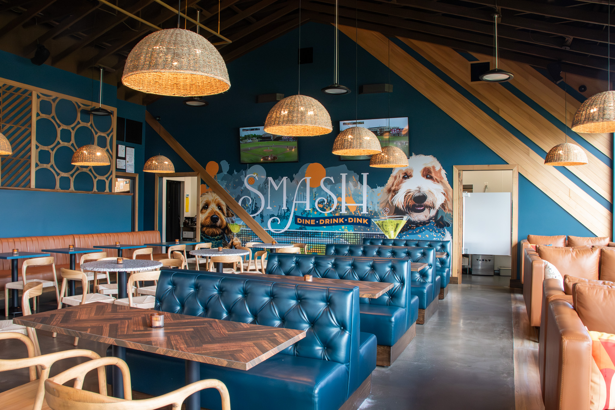 Main indoor dining room with blue tufted booths, woven pendant lights, and the SMASH mural