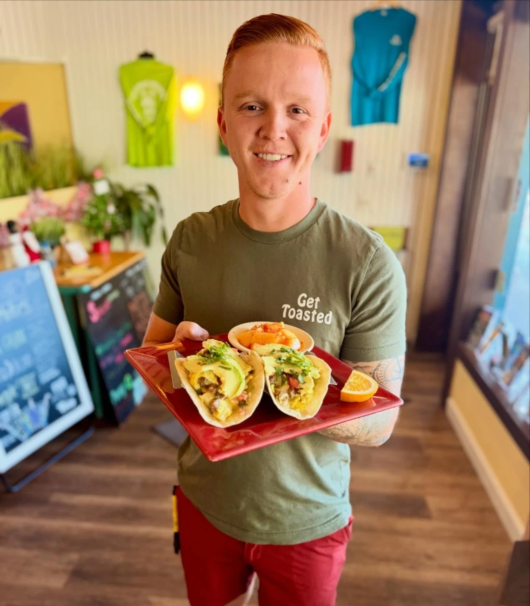 Man holding breakfast tacos with fruit inside Toasted Mango Cafe restaurant
