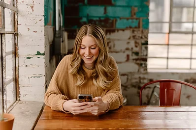 Customer smiling while reading a text message at a table