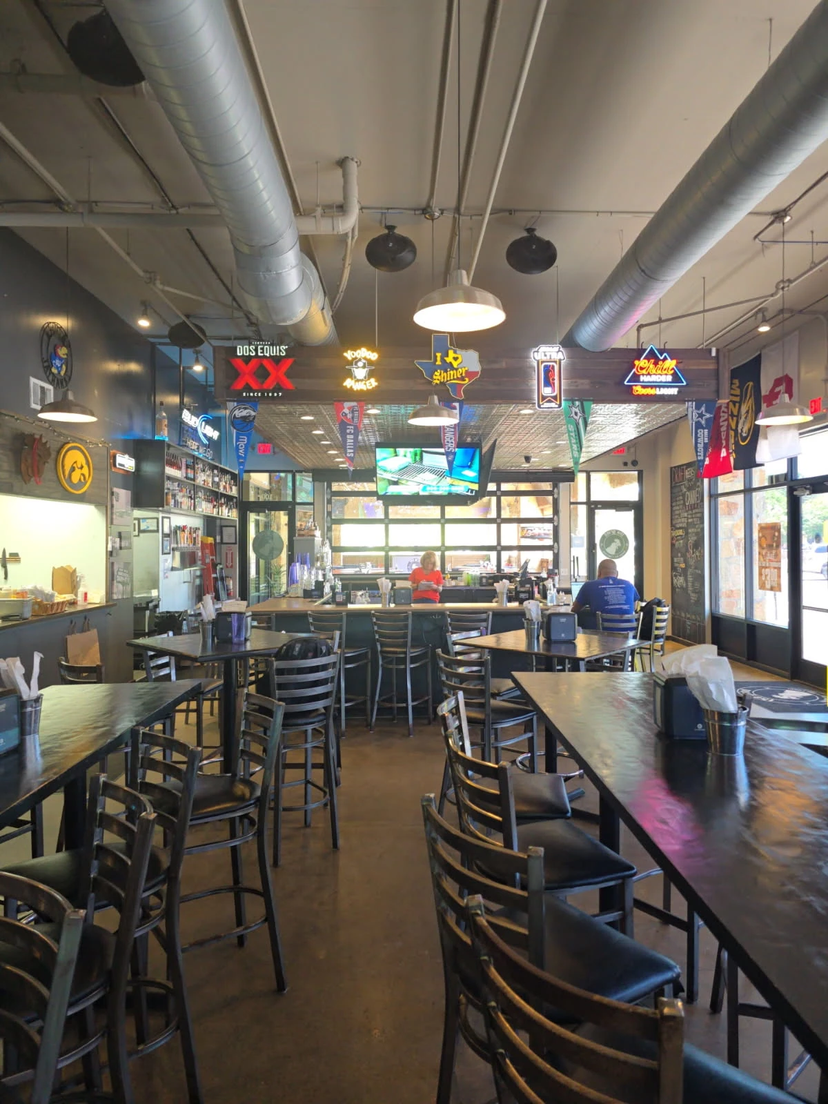 Sports bar dining area with high-top tables, bar seating, and neon beer signs