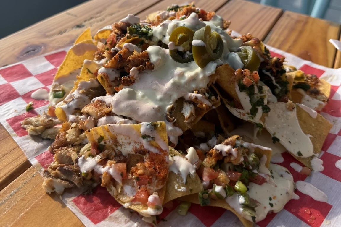 Loaded chicken nachos topped with jalapeños, sour cream, creamy sauce, pico de gallo, and fresh herbs on a wooden patio table