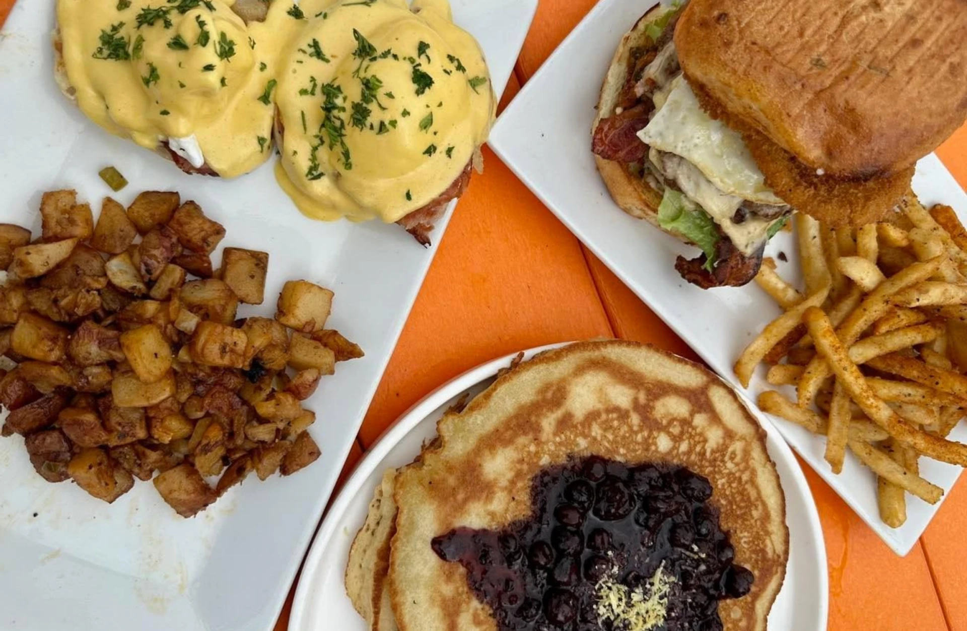 Brunch spread at Cargo TX with eggs Benedict, breakfast potatoes, a bacon cheeseburger with fries, and blueberry pancakes