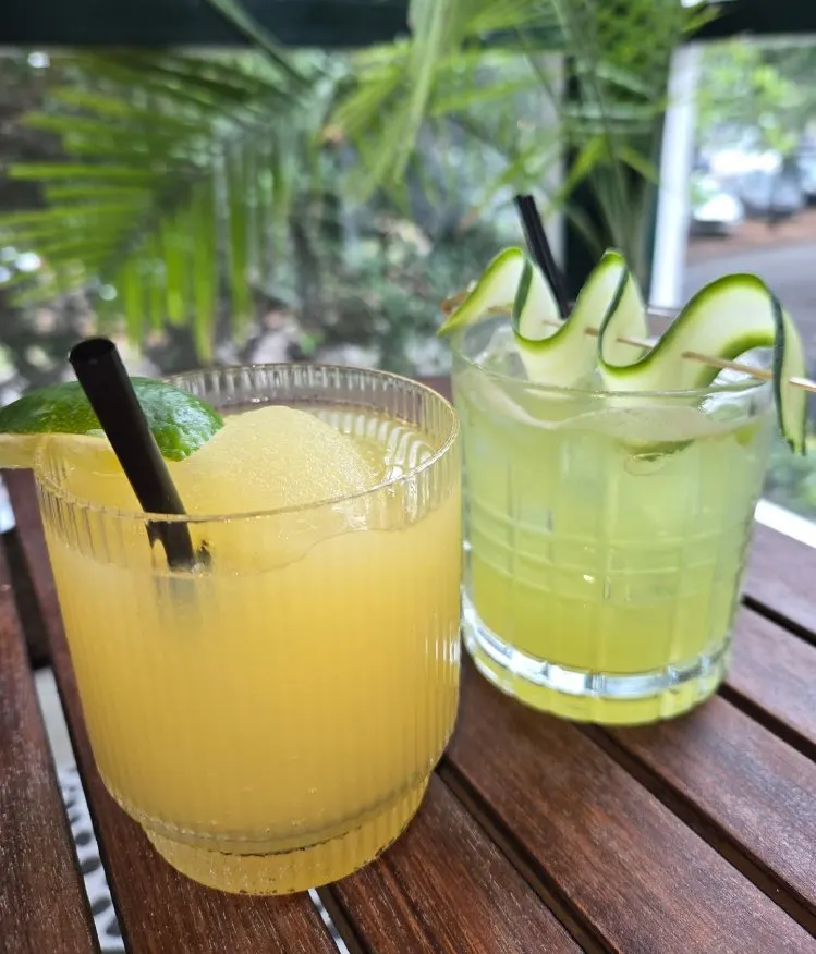 Two tall citrus cocktails garnished with mint and served with straws on the balcony