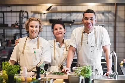Restaurant kitchen team smiling together behind a prep counter with fresh ingredients