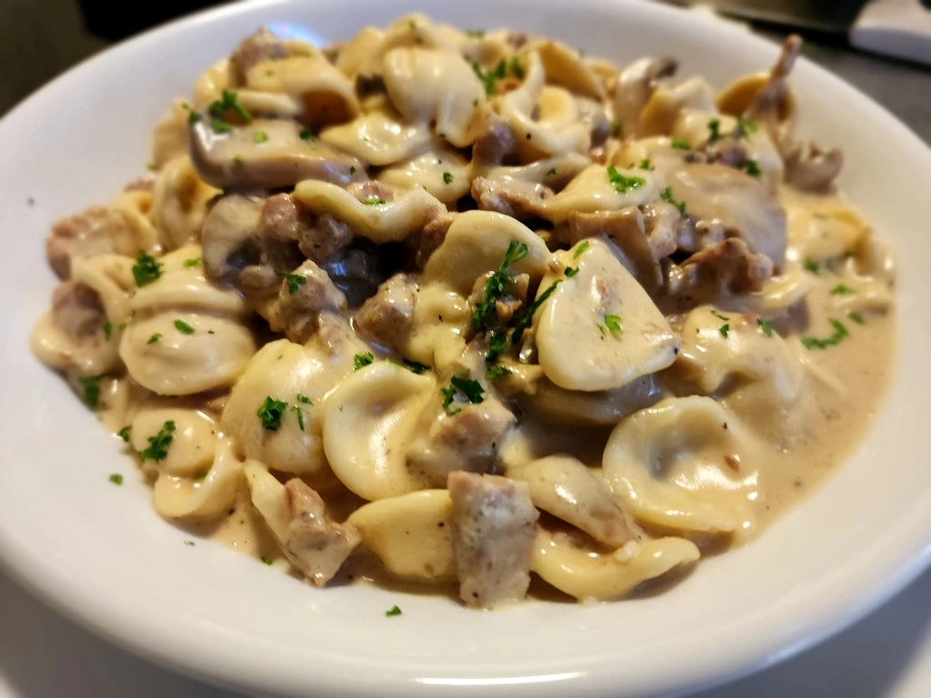 Creamy orecchiette pasta with mushrooms and sausage, topped with fresh parsley and served in a white bowl.