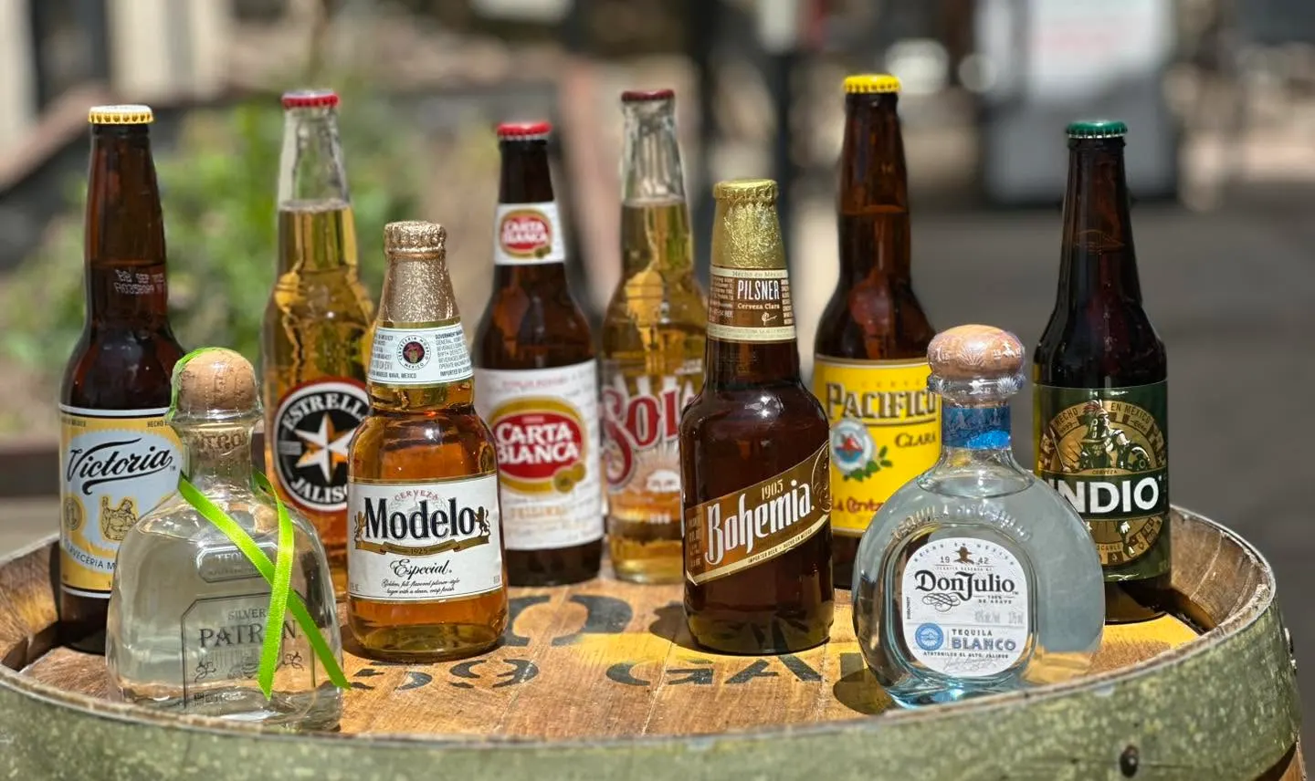 Mexican beers including Modelo, Pacifico and Victoria arranged with Patrón and Don Julio tequila on a wooden barrel