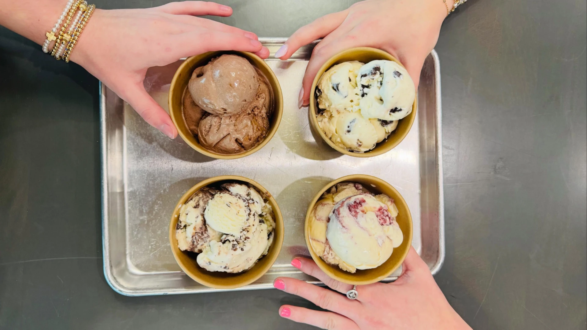 Four bowls of handcrafted ice cream on a tray with people reaching for them