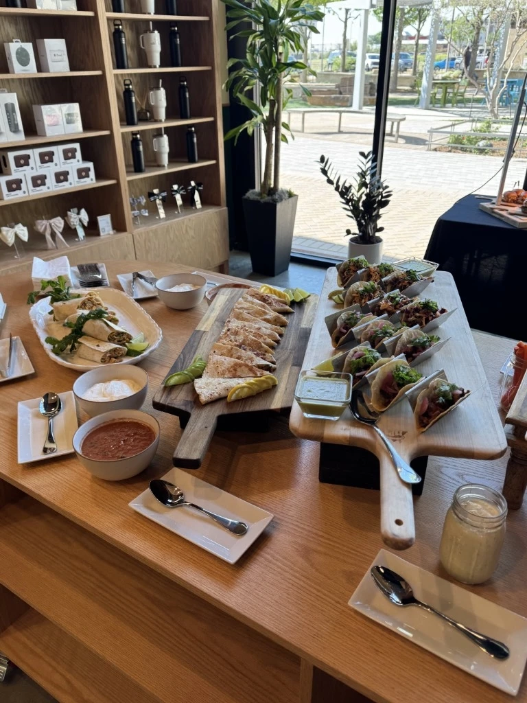 Modern catering display with tacos, quesadillas, wraps, dips, and fresh garnishes served on wooden boards near large windows