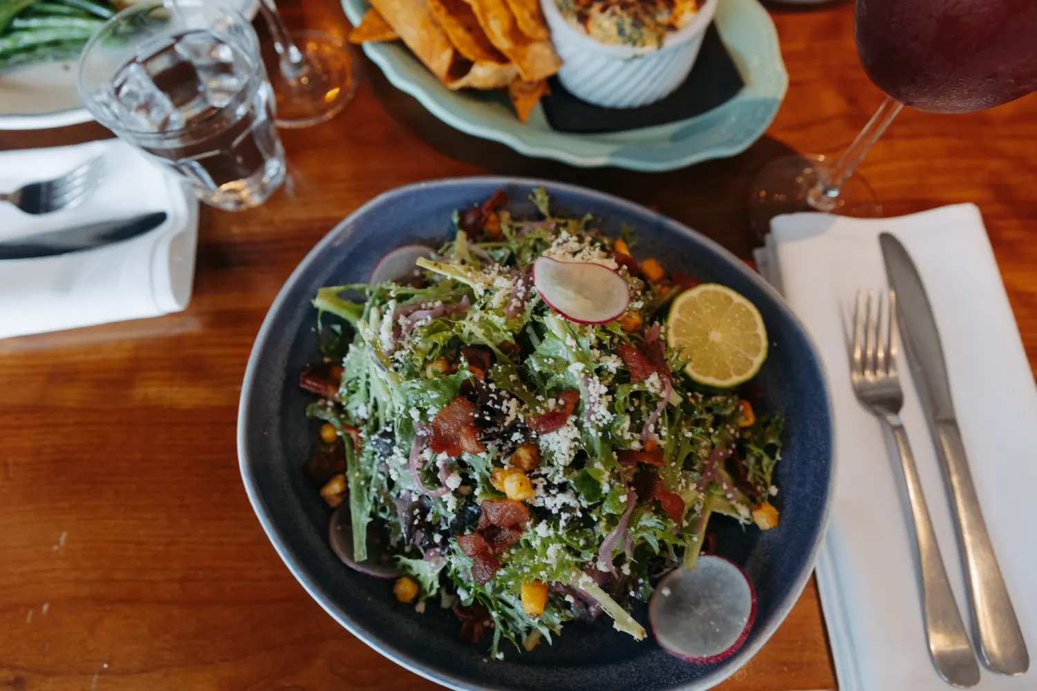 A salad served in a dark blue bowl with a lemon wedge and a side of fries at Junior’s on Harrison