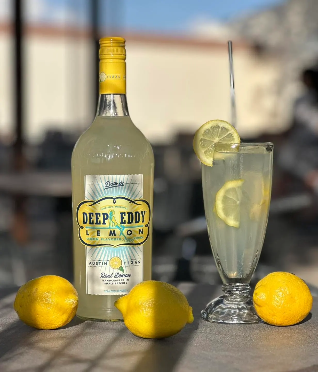 A bottle of Deep Eddy Lemon vodka beside a lemon cocktail and fresh lemons