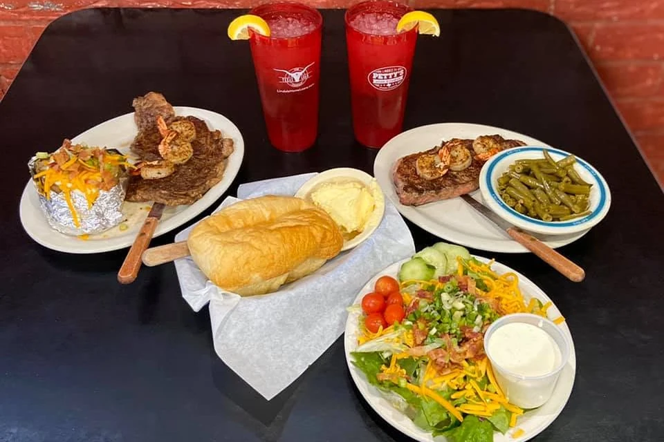 Hand-cut steaks topped with shrimp, served with sides at Petty's
