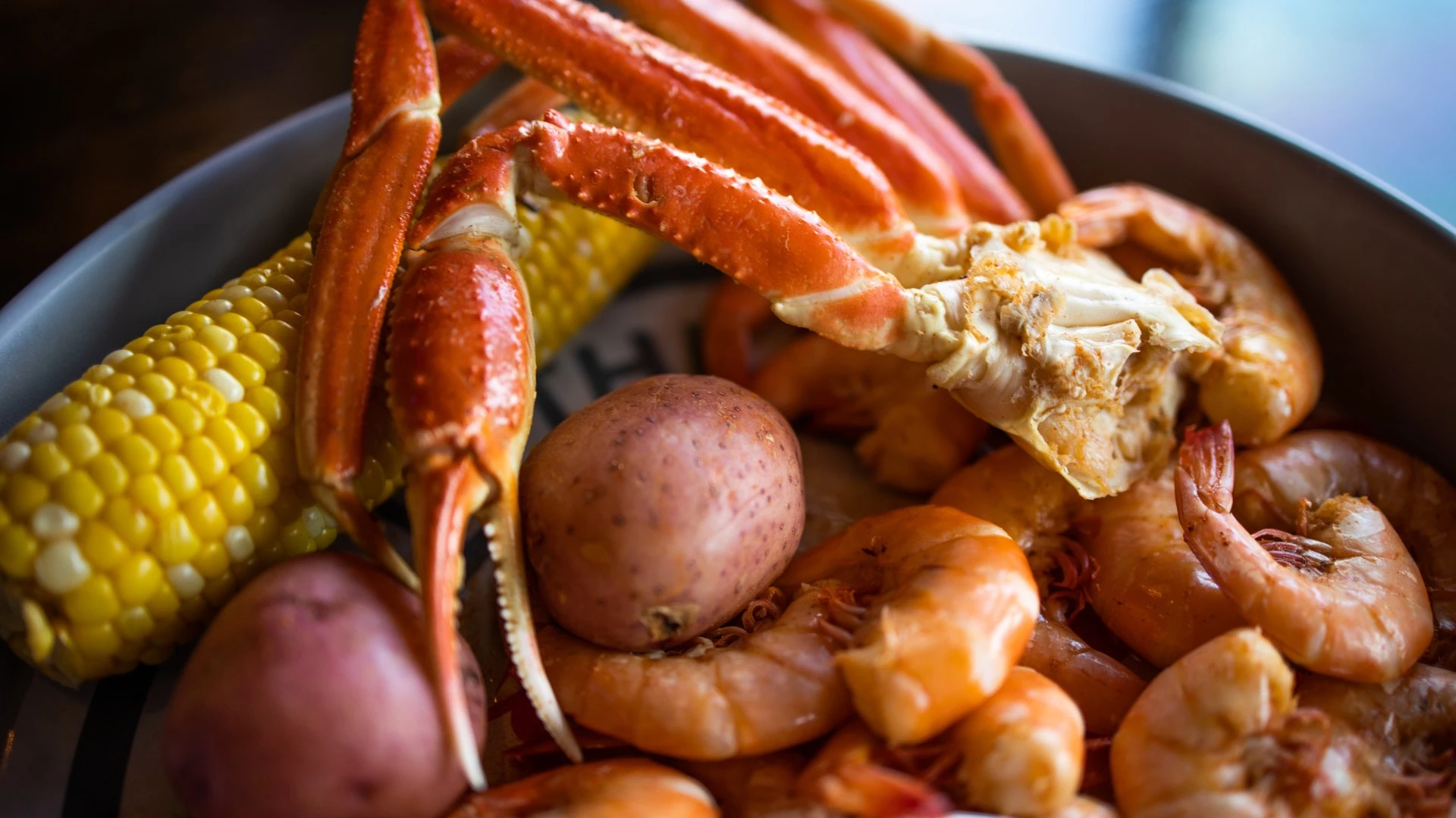 Boiled snow crab legs served with shrimp, corn on the cob, and red potatoes in a seafood platter.