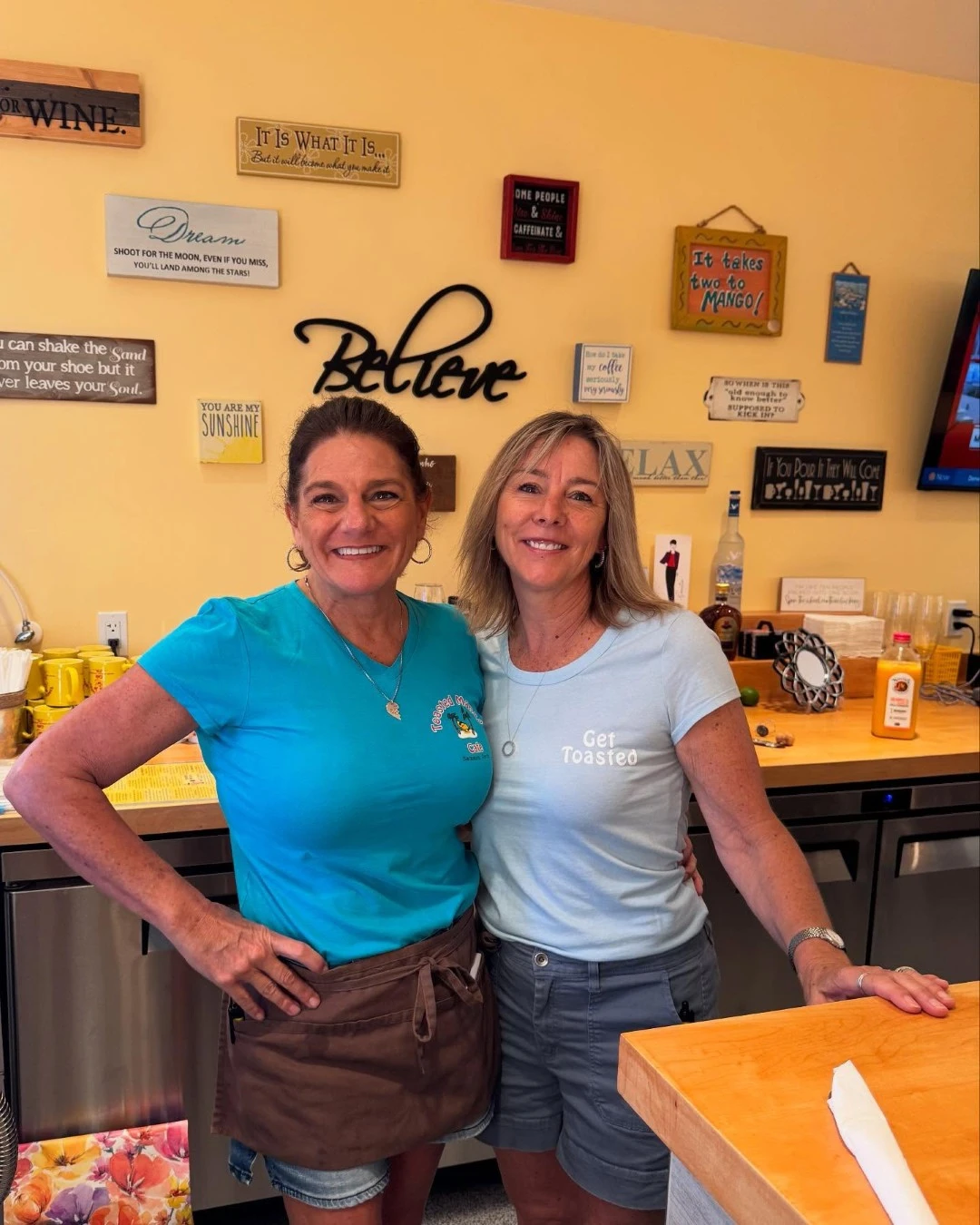 Two staff members smiling inside Toasted Mango Cafe with colorful wall decor