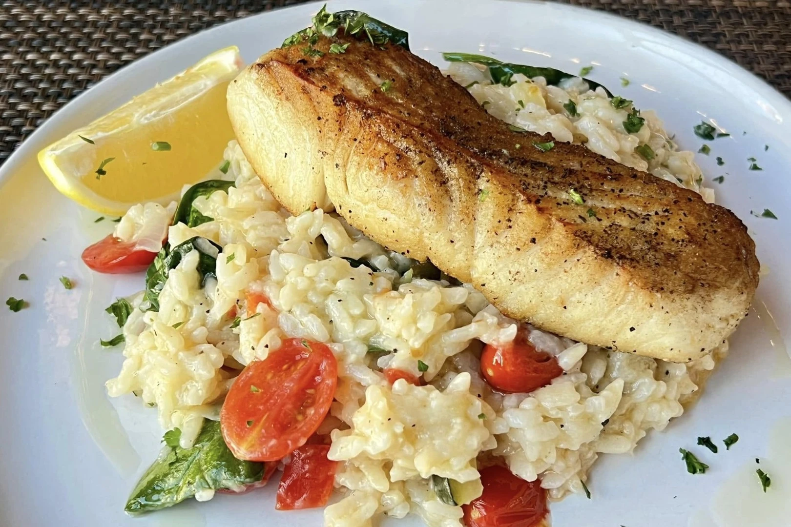 Grilled salmon served over creamy risotto with cherry tomatoes, spinach, and a lemon wedge