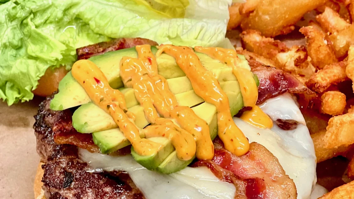Burger topped with avocado, bacon and melted cheese