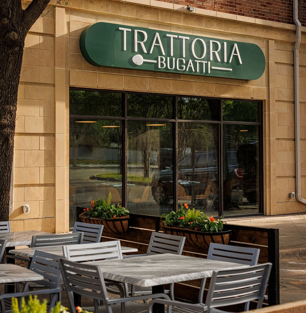 Outdoor patio seating in front of Trattoria Bugatti restaurant with tables, chairs, and greenery