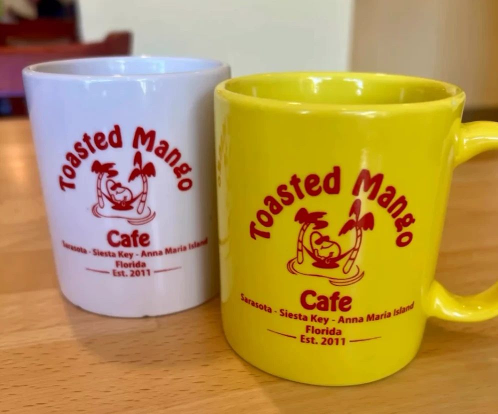 Toasted Mango Cafe branded coffee mugs in yellow and white on wooden table
