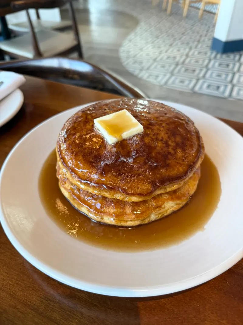 A stack of pancakes topped with a pat of butter and syrup, served on a white plate at Junior’s on Harrison