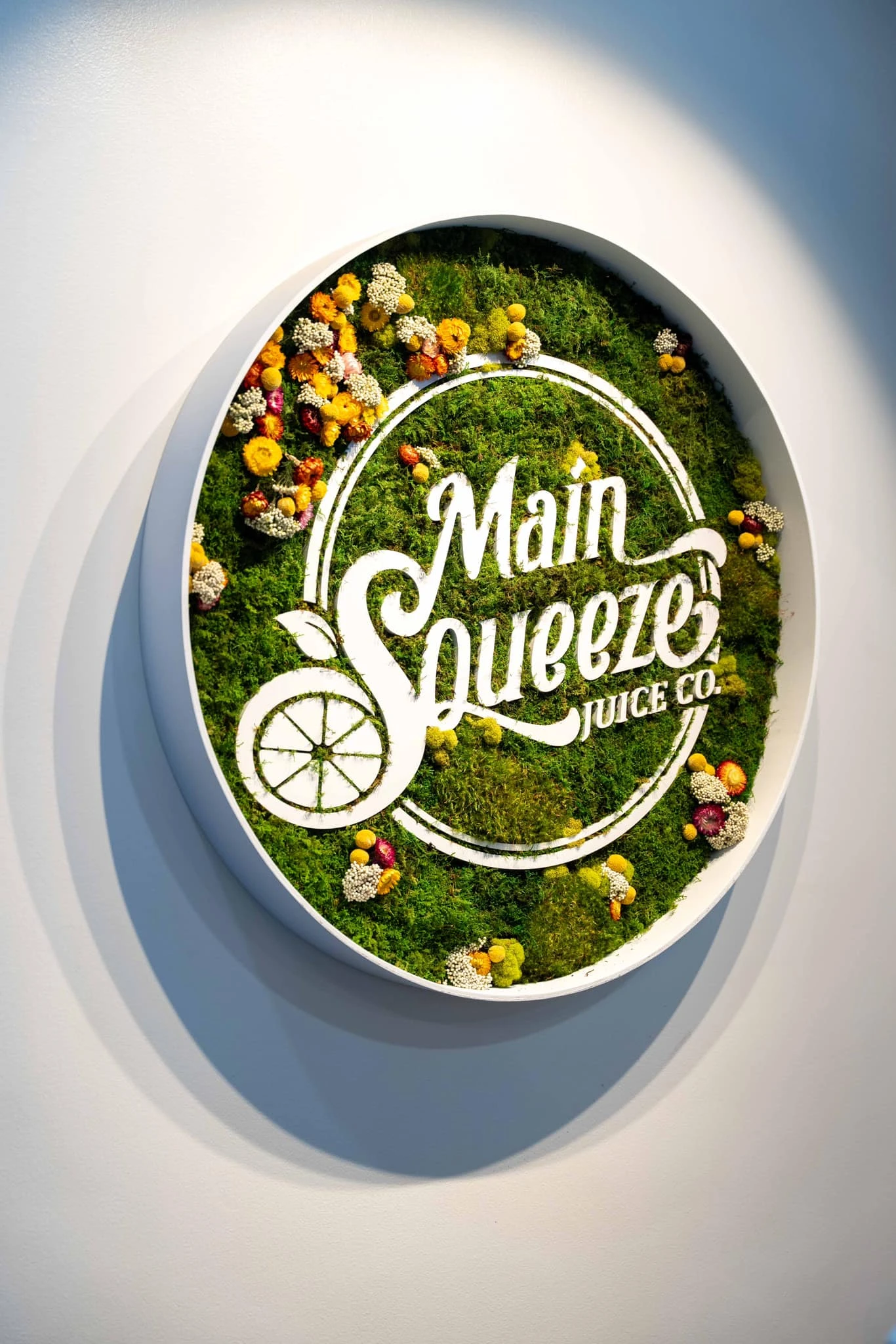 Main Squeeze Juice Co. logo art made of preserved moss and dried flowers on a wall display