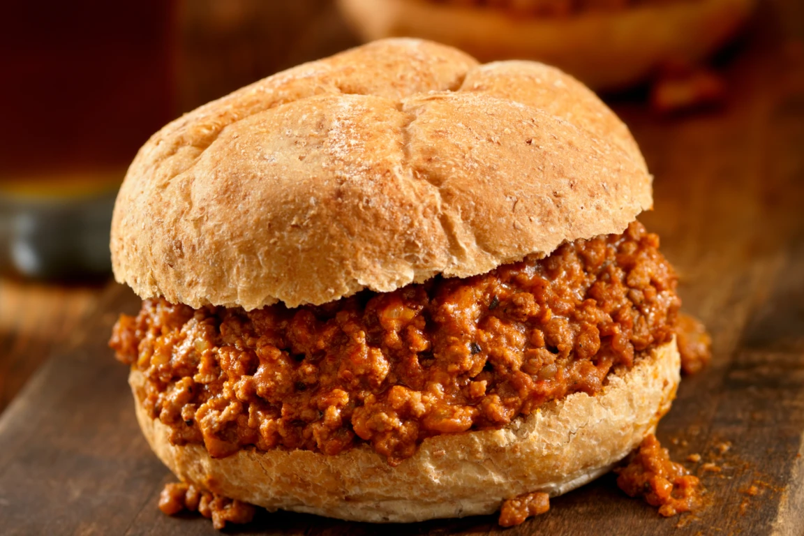 Close-up of a sloppy joe sandwich on a rustic bun with seasoned meat filling on a wooden table