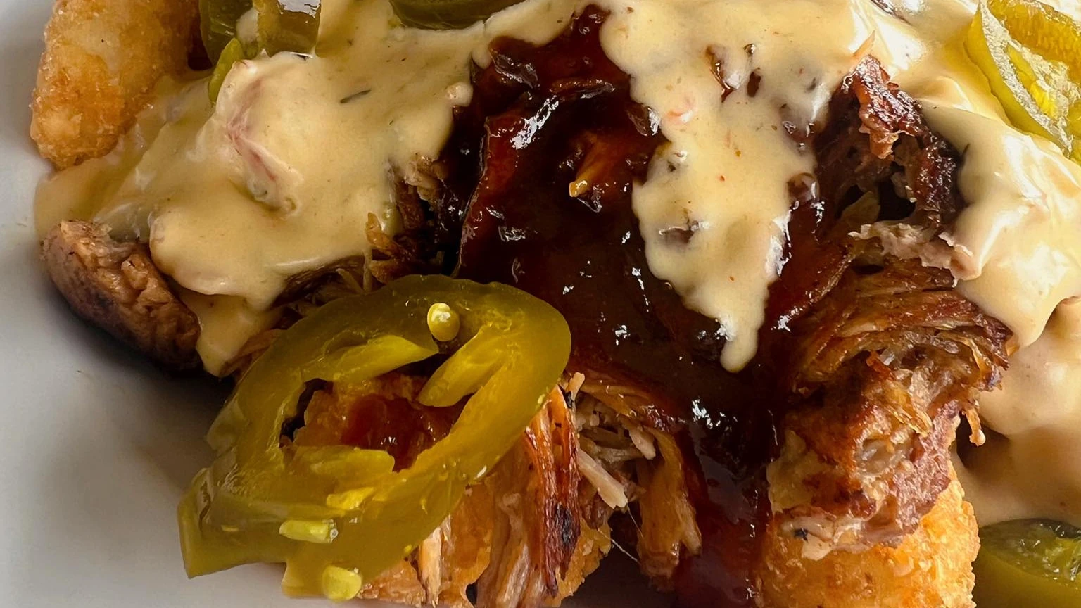 Barbecue pulled pork nachos topped with white queso, barbecue sauce and sliced jalapeños.