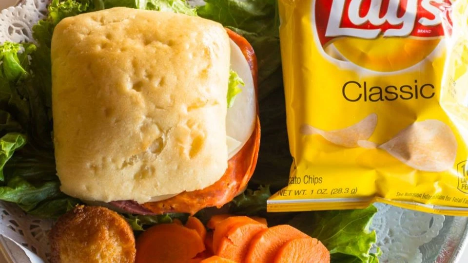 Ciabatta sandwich with deli meats and lettuce served with sliced carrots, a small muffin, and a bag of Lay’s Classic potato chips