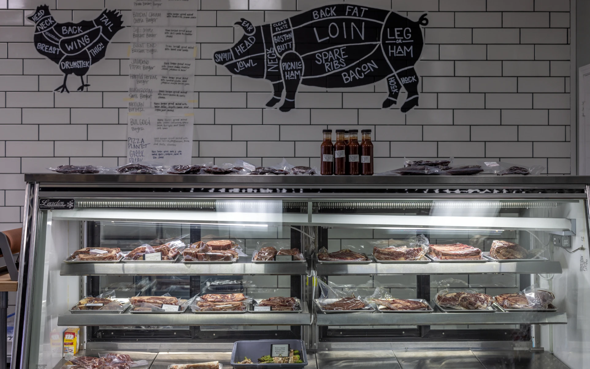 Interior meat display case at The Meatatory with butcher cut diagrams on the wall