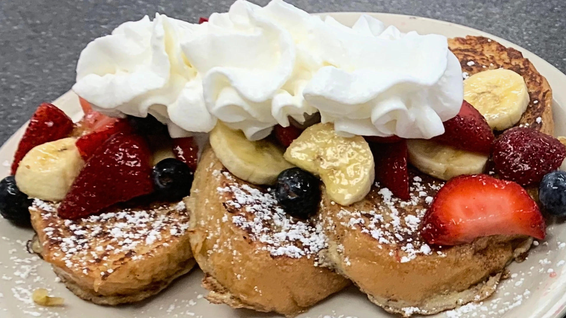 Stuffed French toast topped with whipped cream, strawberries, bananas, and blueberries