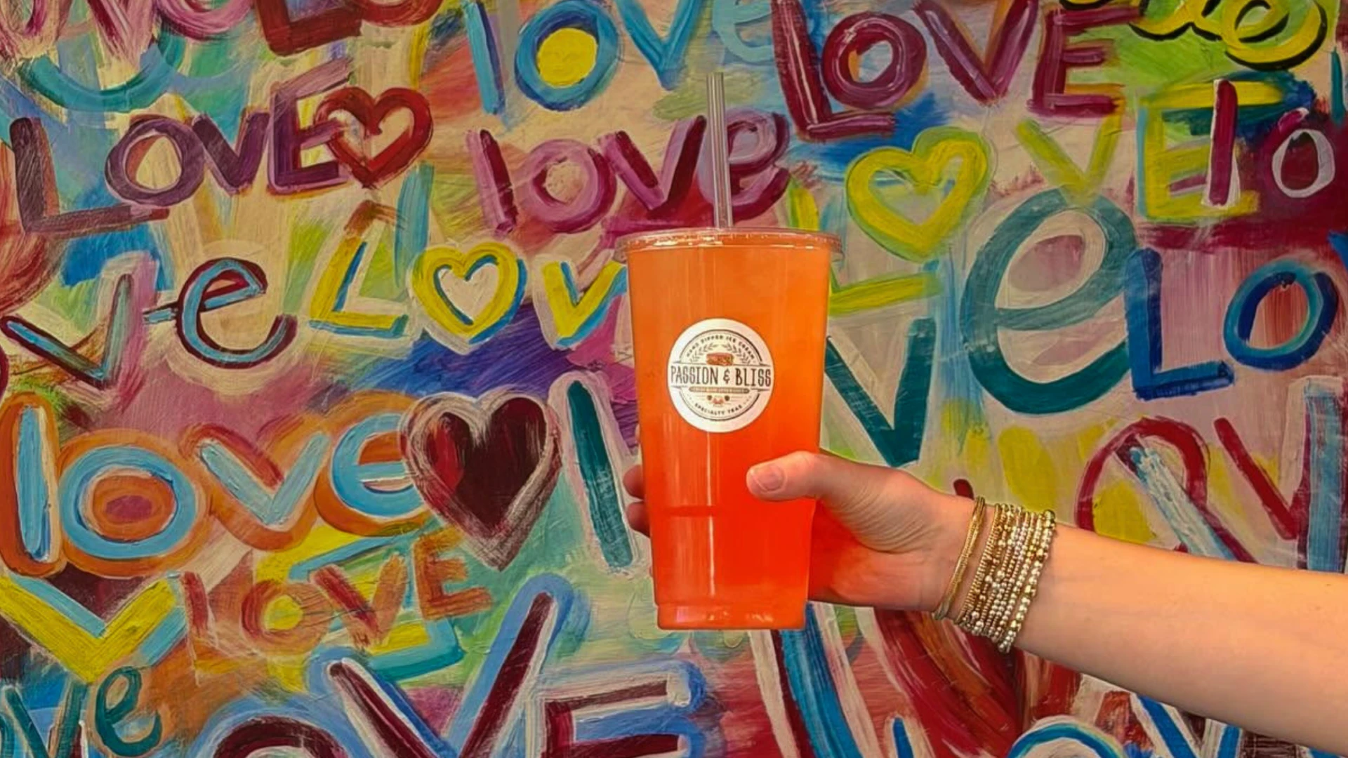 Passion & Bliss signature orange drink held in front of a colorful love mural