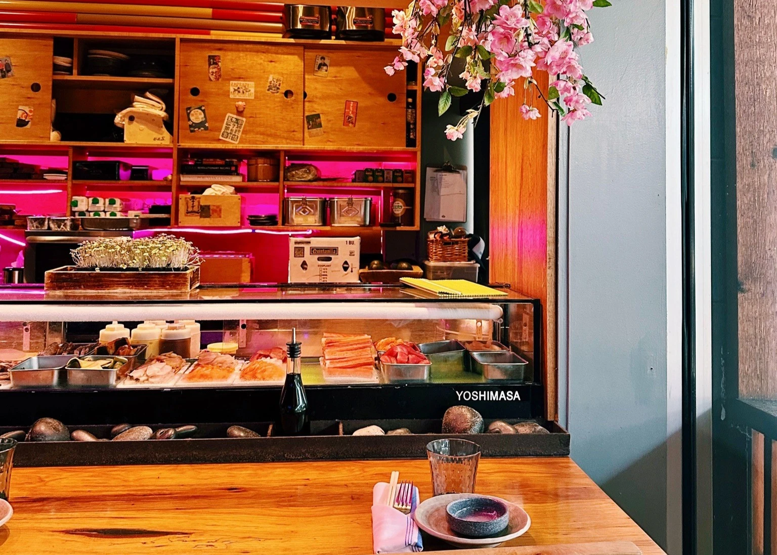 Sushi bar and dining area with fresh seafood display, cherry blossoms, and warm ambient lighting