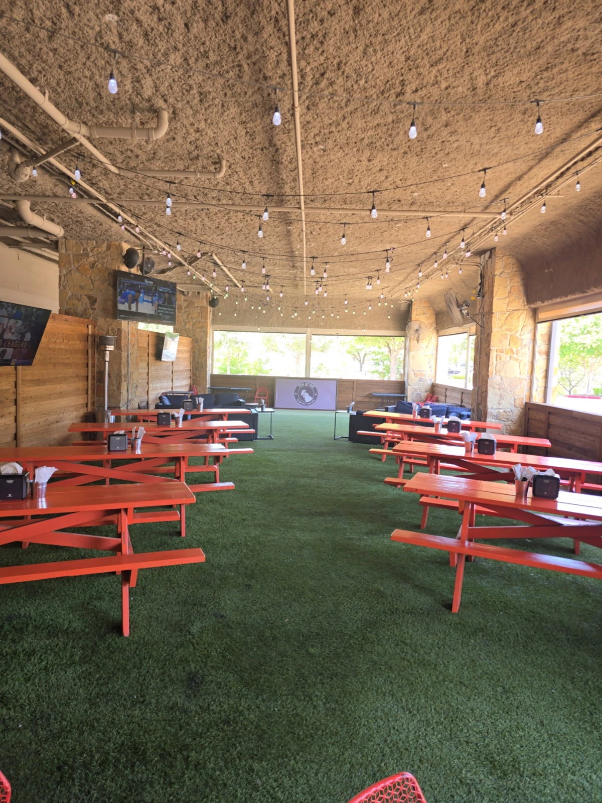 Covered outdoor patio with string lights, picnic tables, and turf flooring