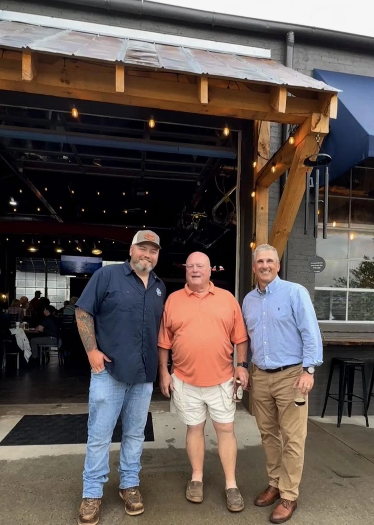 3 people outside the garage door of The Current Tavern
