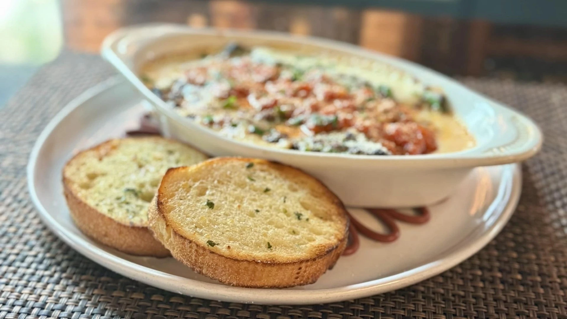 Baked pasta dish topped with marinara, melted cheese, and herbs, served with toasted garlic bread