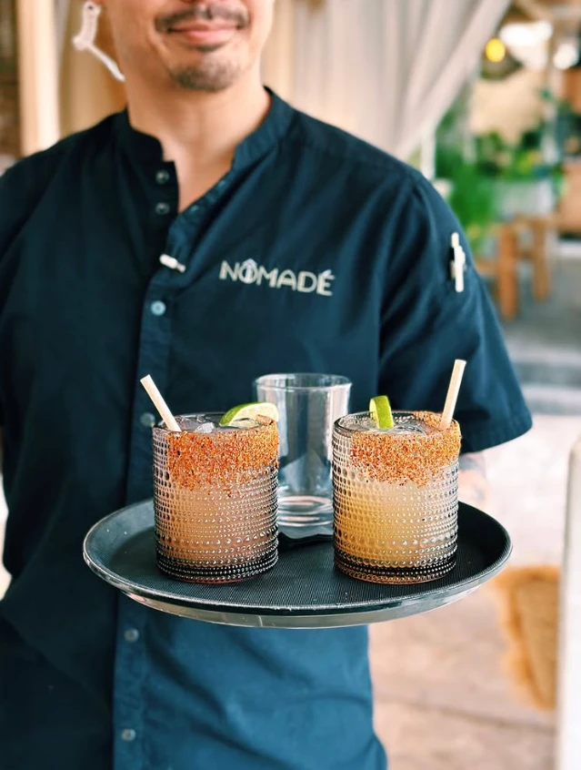 Nomade Cocina server carrying two chamoy-rimmed cocktails on a tray