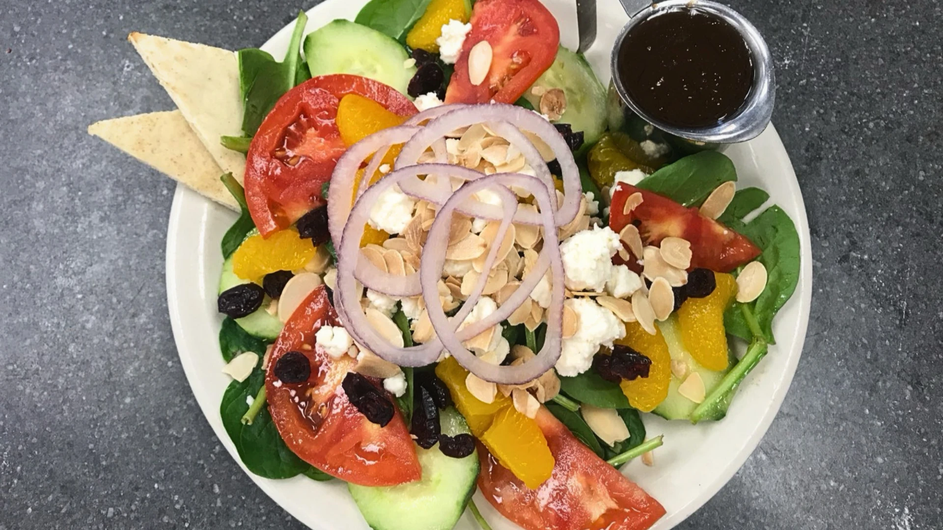Fresh spinach salad with tomatoes, cucumbers, feta cheese, almonds, and citrus slices