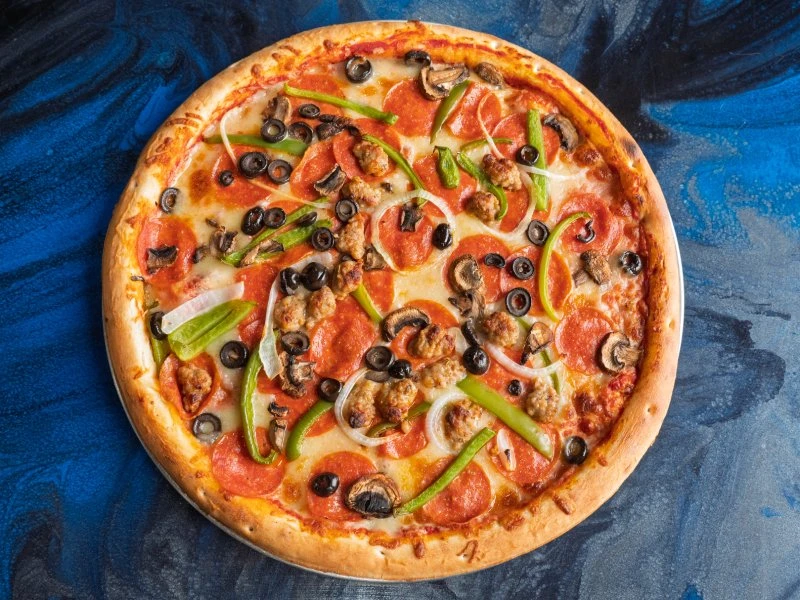Pizza topped with pepperoni, sausage, mushrooms, black olives, onions, and green peppers