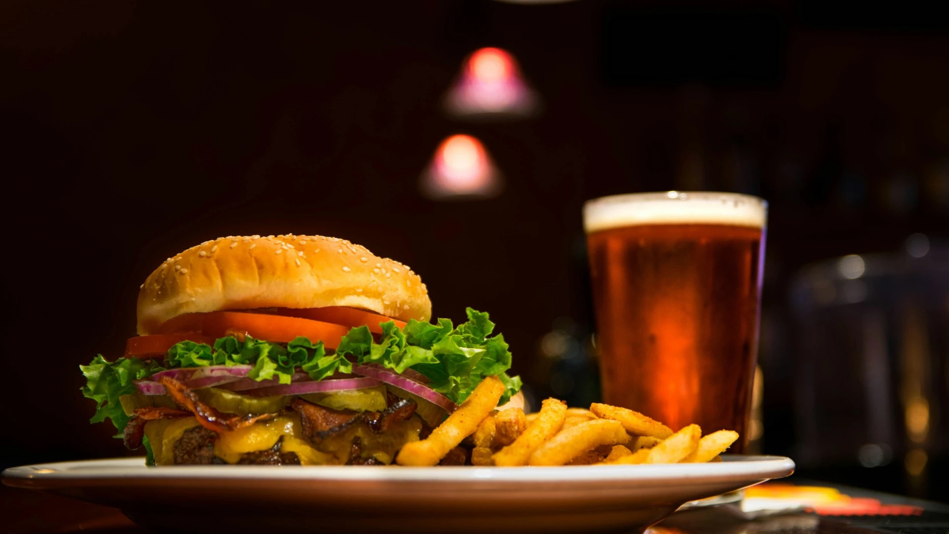 Bacon cheeseburger topped with lettuce, tomato, red onion, and pickles, served with French fries and a pint of beer.