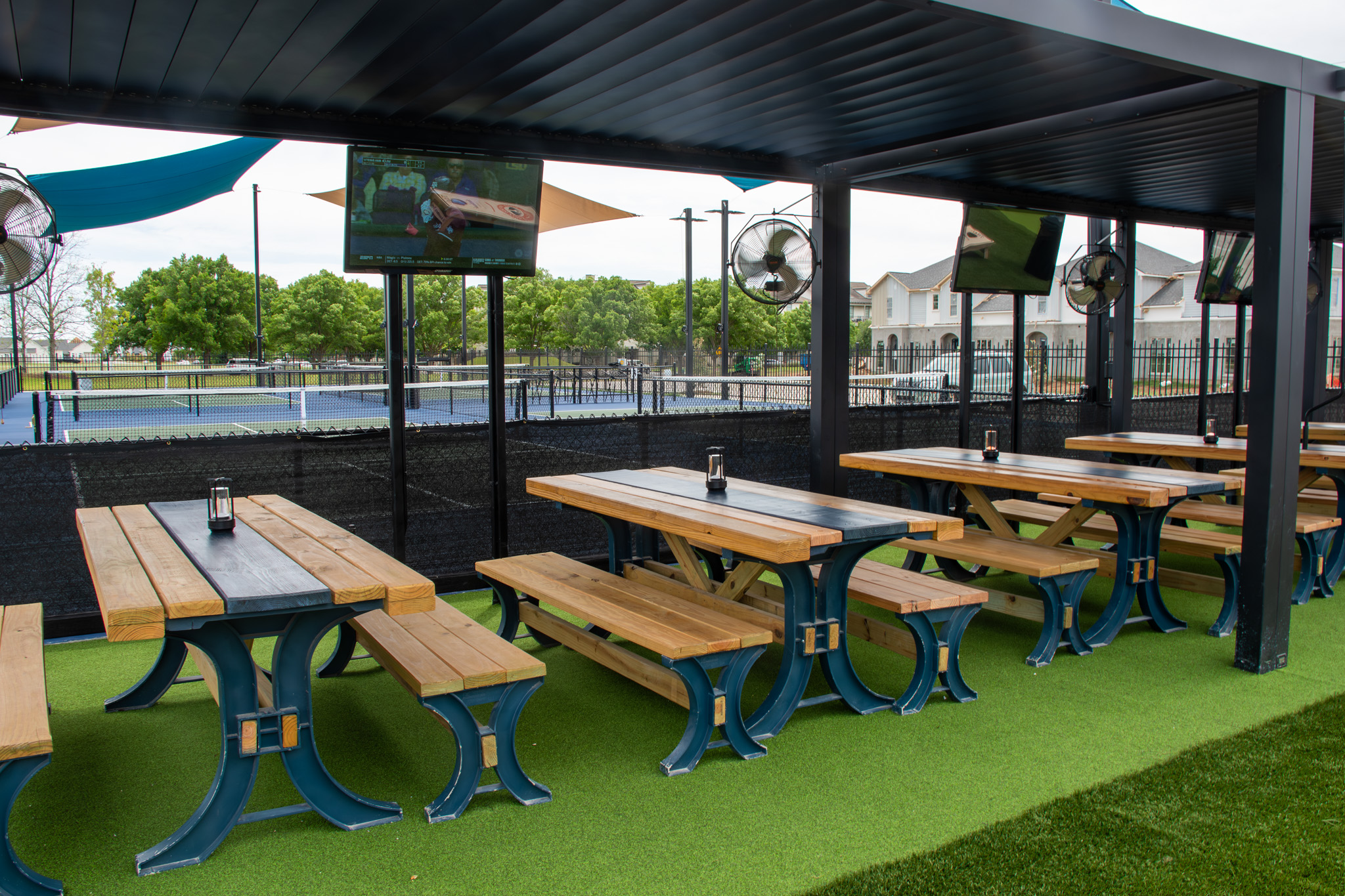 Pergola with picnic tables, wall fans, and TVs beside the pickleball courts