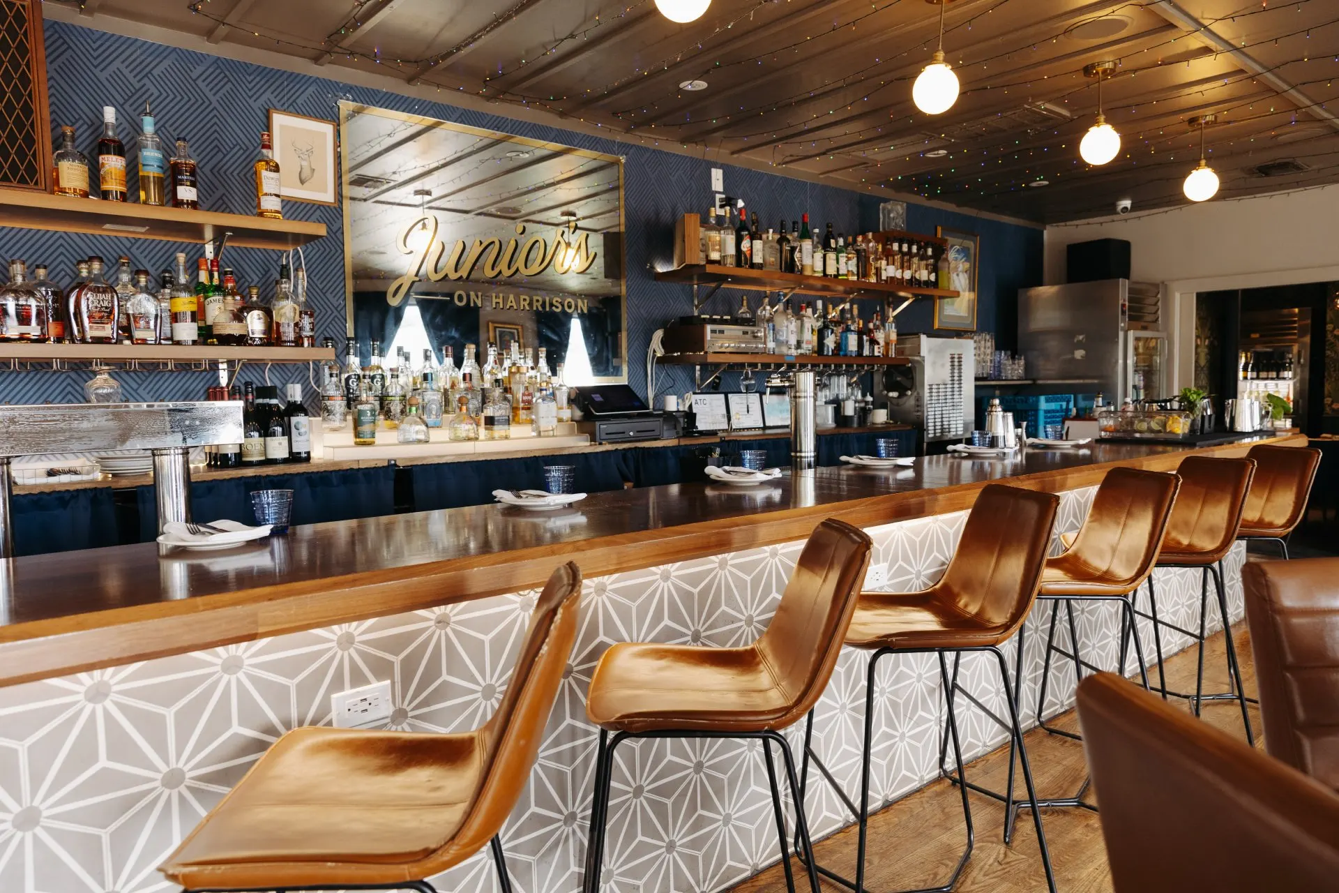 The bar at Junior’s on Harrison with rattan stools, woven pendant lights and blue and white patterned tile floor
