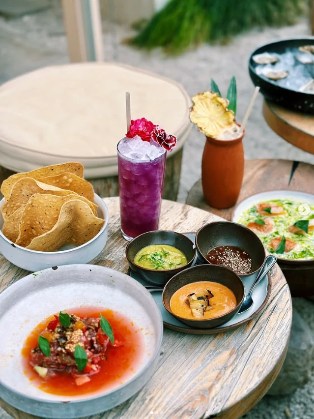 Tostadas, ceviche, and a purple cocktail on a wooden table at Nomade Cocina