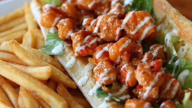 Buffalo popcorn shrimp po'boy topped with lettuce and drizzled with creamy sauce, served with French fries.