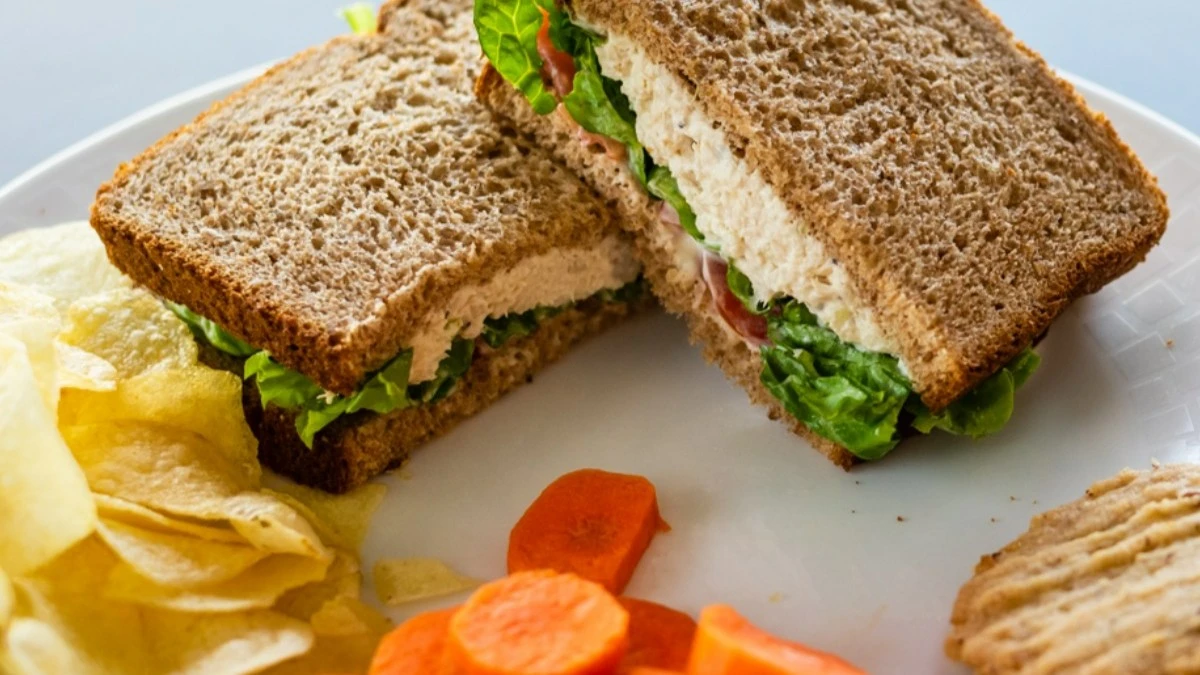 Tuna salad sandwich on whole wheat bread with lettuce and tomato served with potato chips and sliced carrots