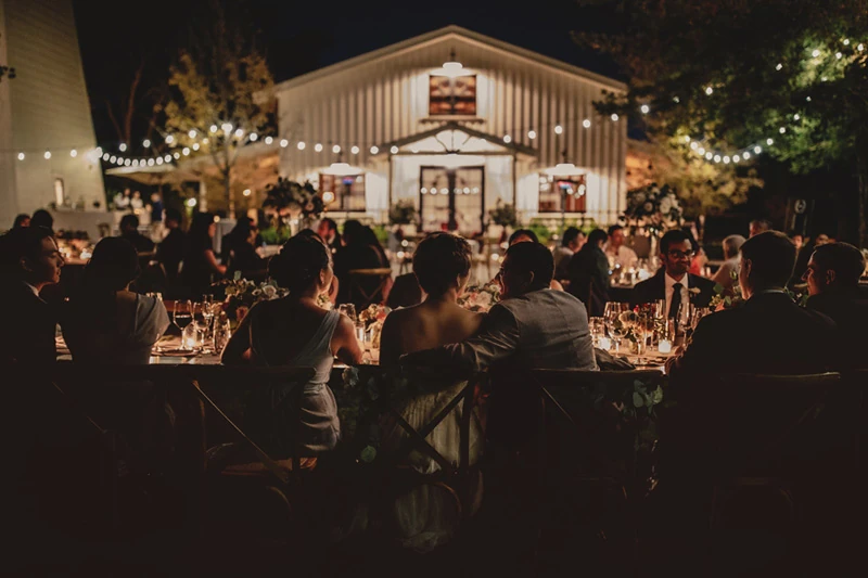Guests seated at long tables at an evening reception under string lights