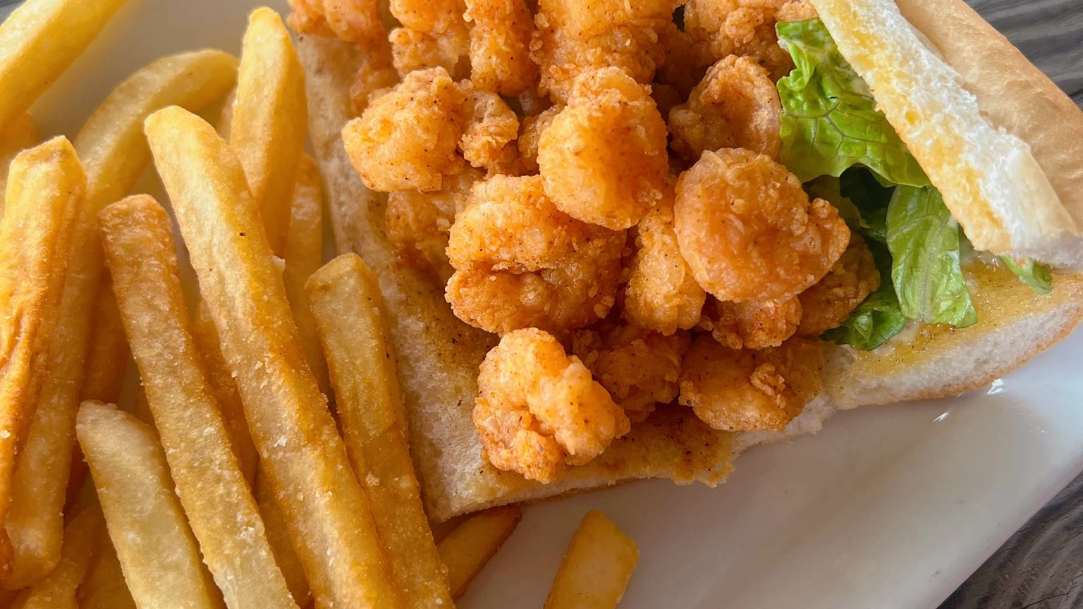 Fried popcorn shrimp po'boy sandwich with lettuce served with French fries.