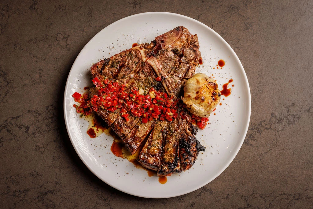 Grilled steak with roasted garlic and red pepper topping on a white plate