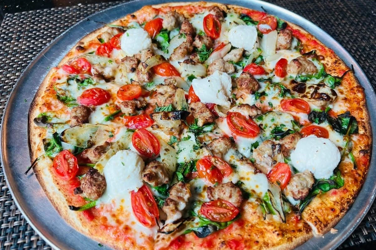 Thin-crust pizza topped with sausage, cherry tomatoes, fresh mozzarella, spinach, and roasted vegetables