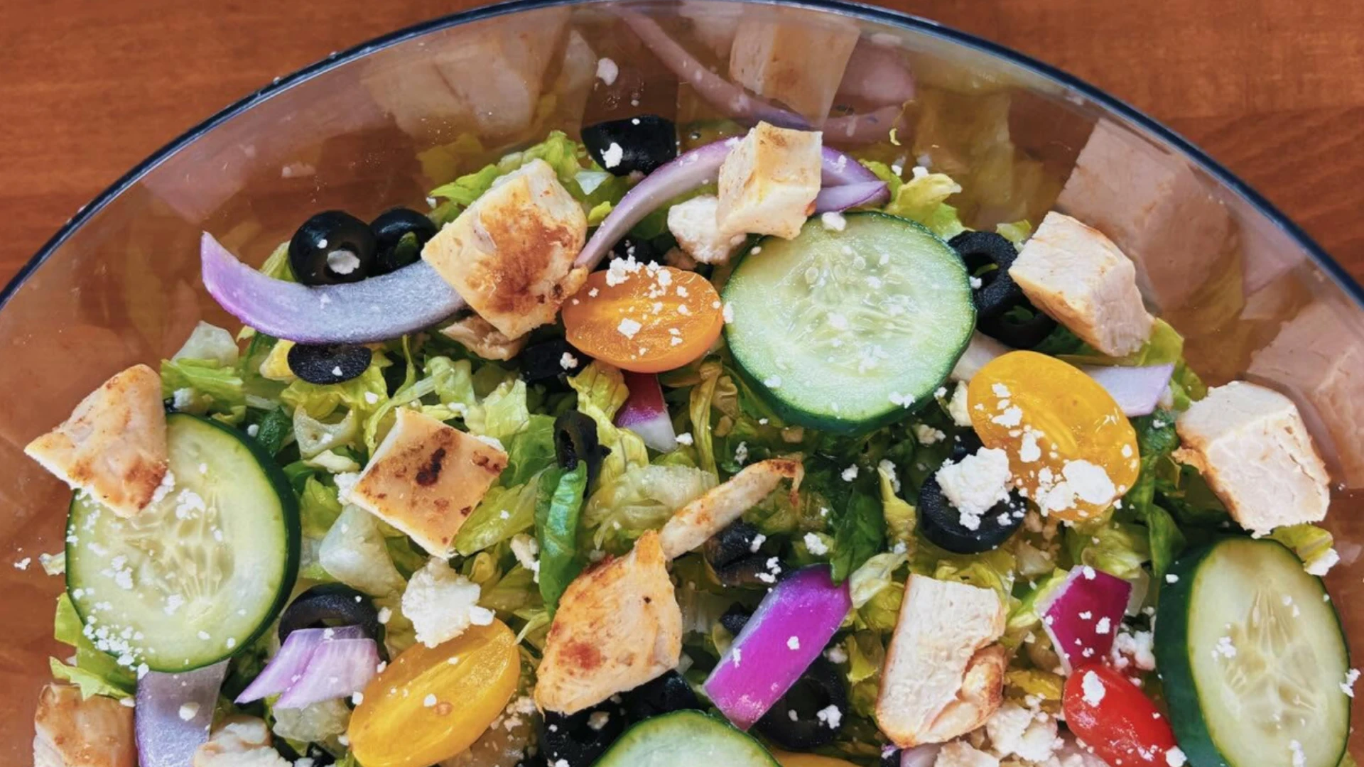 Fresh Greek salad with grilled chicken, cucumbers, tomatoes, olives, feta, and red onion