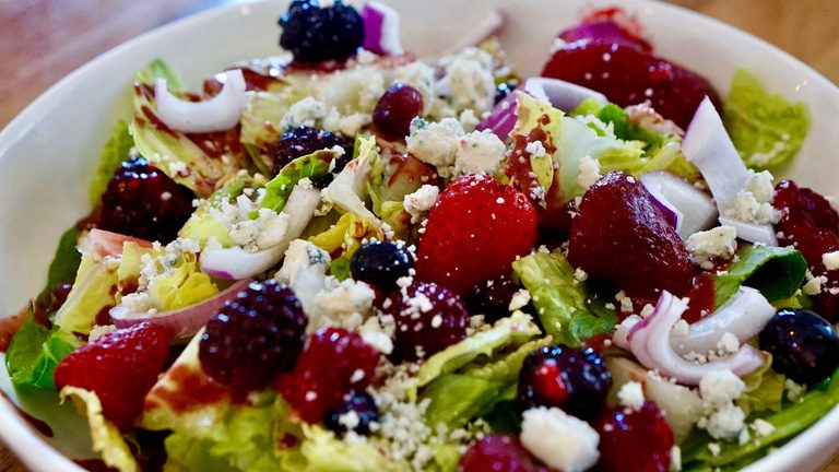 A salad of mixed greens with berries, red onion and crumbled cheese