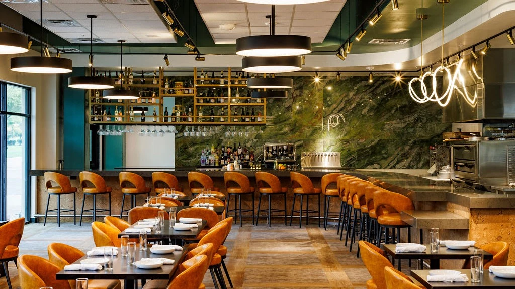 Modern restaurant interior with bar seating, green marble wall, and warm lighting